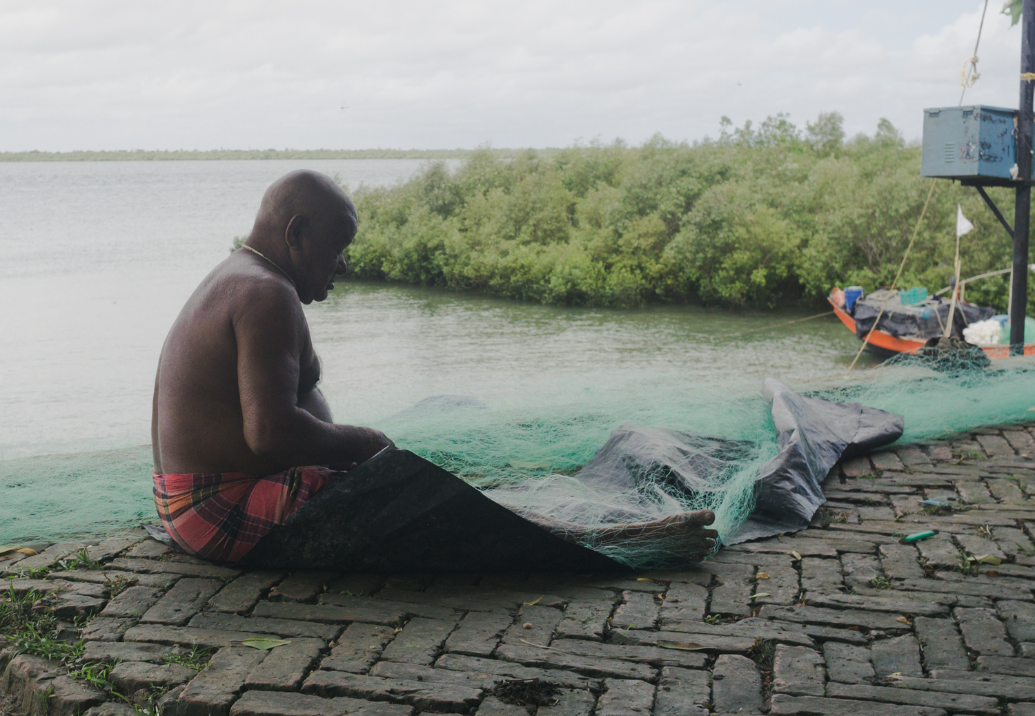 A fisherman mends his net on the bank of river                        
Thakuran.
